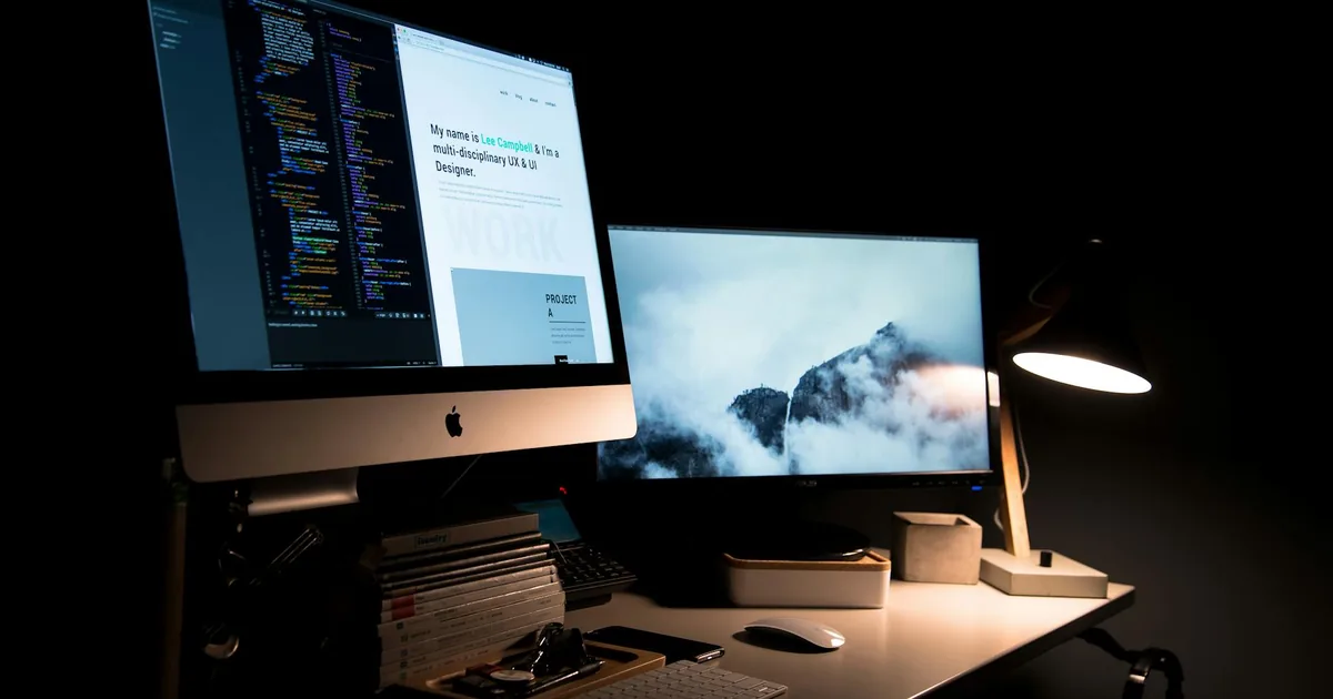 A desk with a desktop computer, laptop, and task light